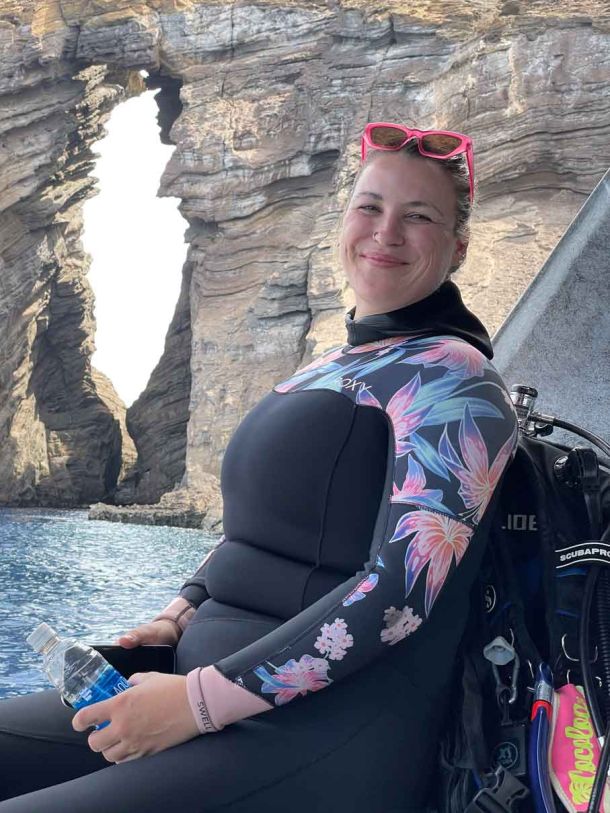 Happy scuba diver wearing a wetsuit posing for a photo infront of the Keyhole on Lehua, Niihau