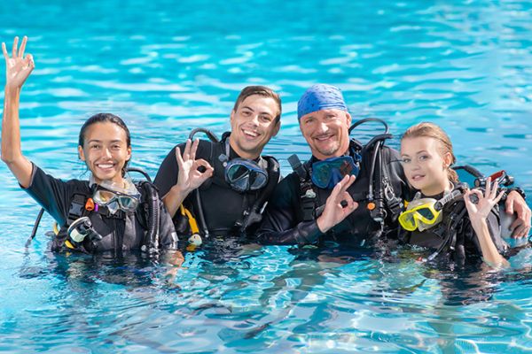 Four scuba divers in the pool giving the "ok" sign with happy faces after a scuba diving class