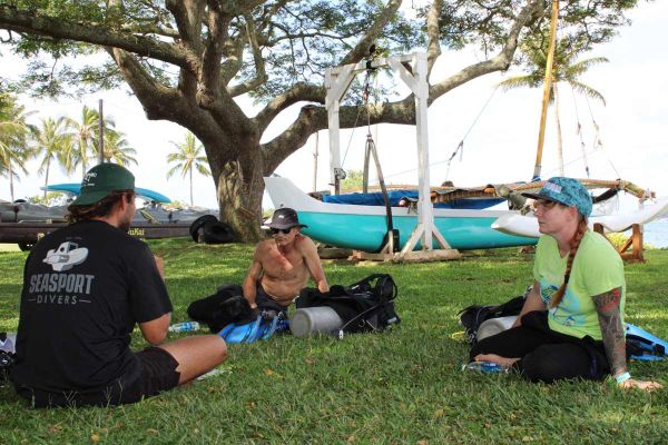 PADI scuba diving Instructor teaching a class on land with students sitting with scuba equipment next to them